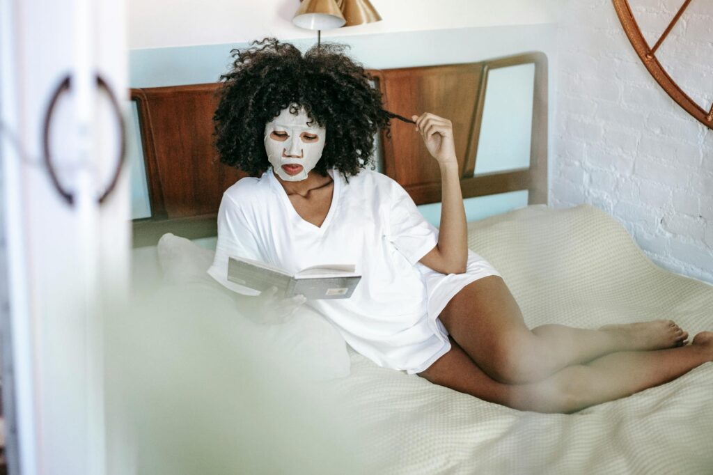 young black lady reading book on bed during skin care routine at home