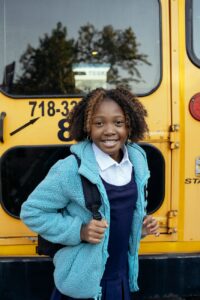 happy black schoolgirl with backpack standing near school bus